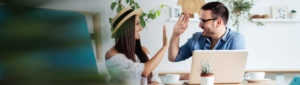 Young adult couple sitting together at table looking at laptop and high-fiving each other