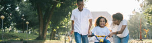 african american family with young daughter teaching her how to ride bicycle