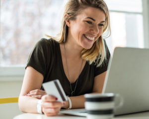 Young female shopping online using laptop holding debit card and smiling