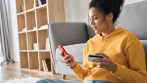 african American female young adult sitting on floor by couch with smartphone and debit card in her hands