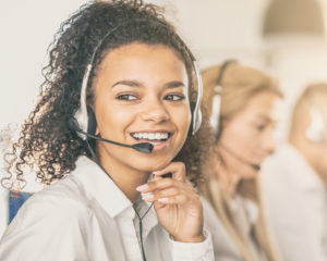 young female adult call center employee smiling as she answers a call on headset phone