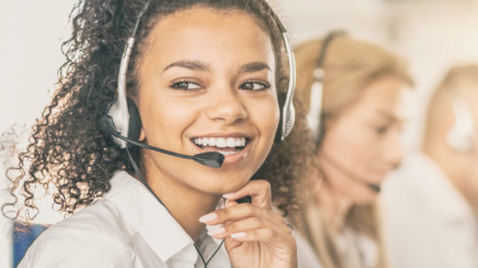young female adult call center employee smiling as she answers a call on headset phone
