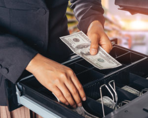 cash register open with business owner placing cash inside