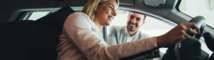 young female adult car shopping with happy car salesman showing her new car