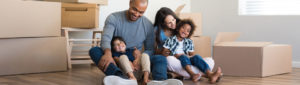 Young adult family with two young children sitting on floor of new home, taking a break while moving boxes in