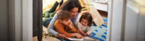 Mother with her two children, one boy one girl under her arms laying together on floor reading a book