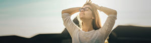 Young adult female smiling and taking a deep breath with arms raised above head