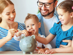 family all gathered around a piggy bank watching younger children place coins into piggy bank