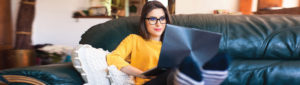 young female adult relaxing on couch with laptop smiling as she pays her bills online