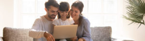 family with young child sitting together on couch looking at laptop computer together