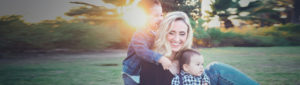 Mother and her two young boys smiling and playing together in a sunny field