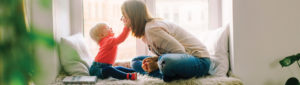 mother and young child sitting together in front of window laughing and playing together