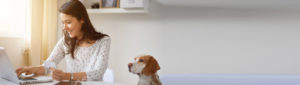 young female adult working at laptop computer with her dog sitting patiently beside