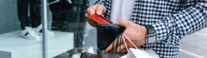 Adult male holding wallet and grabbing debit card, while also holding shopping bags in other hand