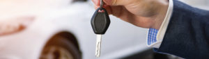 Car salesman holding key to car in front of car in background