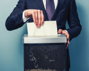 businessman in suit shredding paper with paper shredder machine