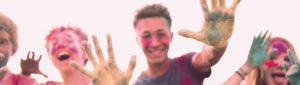 Group of teenage kids covered in multicolored paint powders all laughing and smiling with their hands raised