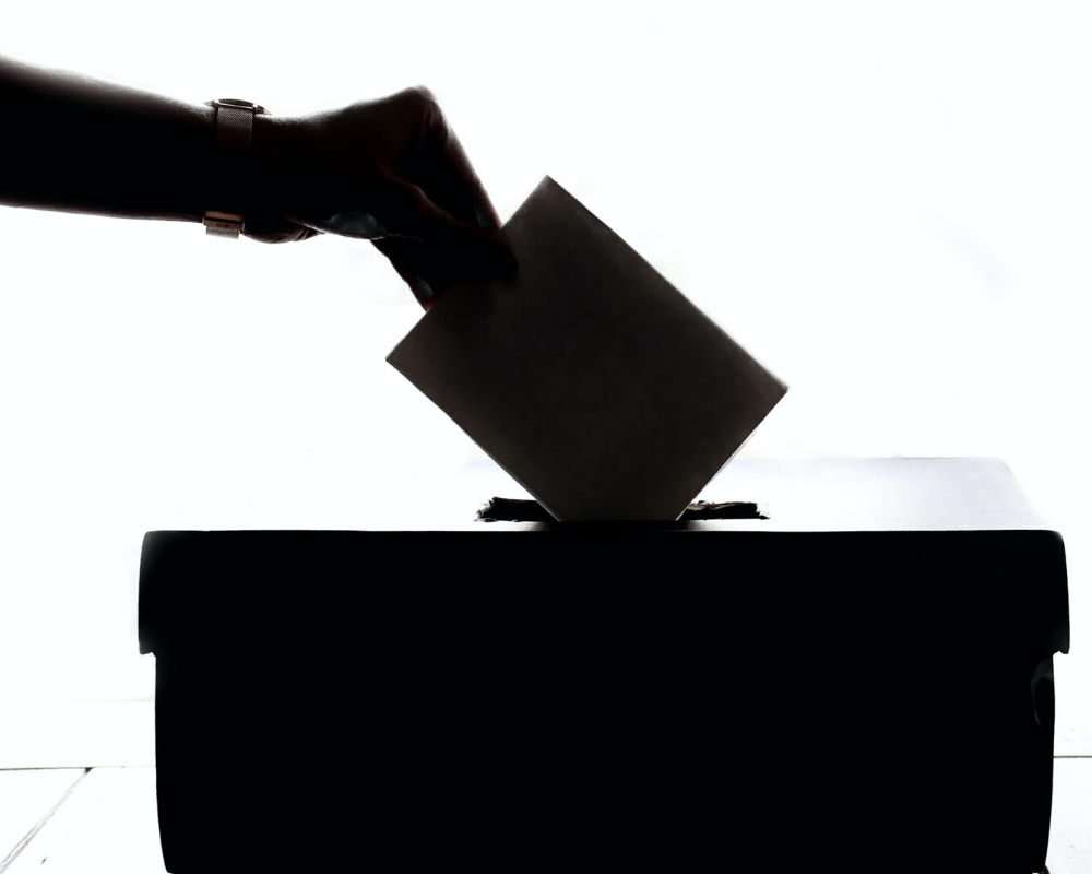Person dropping a piece of paper into a voting ballot box.